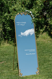A gold-framed mirror welcome sign with white calligraphy for a luxury summer wedding at Diamond Cross Ranch in Jackson, Wyoming.