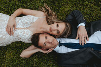 Bride and groom laying in the grass holding each other's face