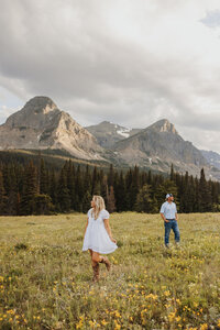Elopement couple walking through a grassy field, looking away from each other, with pine trees and Montana mountains in the distance.