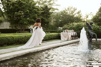 Bride running toward table with black chairs along fountain in the garden at the War Memorial in Grosse Pointe Detroit Michigan