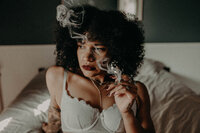 Black Mexican woman with natural curls and dark lipstick, smoking herbal joint, moody and provocative boudoir portrait.