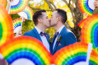 Newlyweds kissing with rainbow fans around them