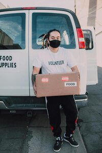 man in mask standing in front of white can holding a care package