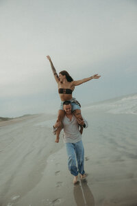 boyfriend giving girlfriend piggyback ride on the beach in jacksonville, florida
