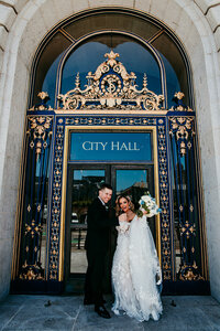 Just married couple celebrating in front of the ornate gold doors at San Francisco City Hall, captured by San Francisco elopement photographer Kristin Smith.