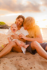 close up image of a young boy laughing with his parents while sitting in the sand on kapalua bay