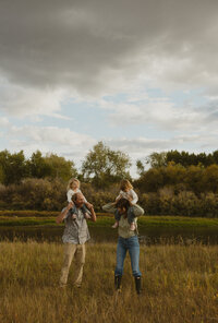 A husband and wife and standing on the edge of a lake. They are holding their son and pointing into the distance.