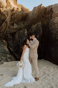 bride and groom embracing on a beach in front of rocks