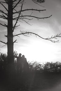 An engaged couple holds one another's faces close and giggle during an intimate moment in the sunset