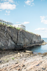Towering rocky cliffs meet the ocean below the Cliff House Maine, with the resort buildings perched dramatically above the rugged shoreline.