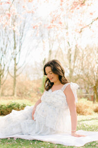 A woman sits on the grass in a white and blue puffy dress.