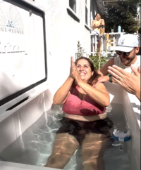 Image of a woman smiling sitting in a cold plunge and being guided by founders Mia and Matt Heck.