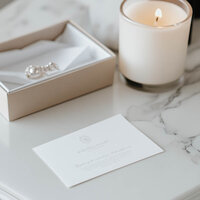Elegant flat lay of Martina Bailey fine art wedding photographer branding card placed on a marble surface with a lit candle and pearl-styled stationery box—luxury branding design for photographers.