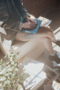 A woman is sitting on a box, with her legs crossed, typing on her laptop in this hazy photo.