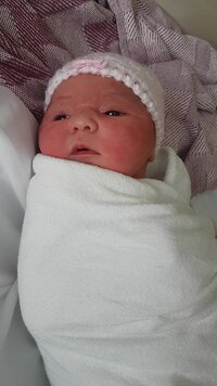 newborn baby girl in a hat swaddled in a blanket