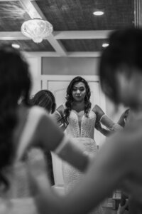 Black and white image of bridesmaids helping bride fix her wedding dress