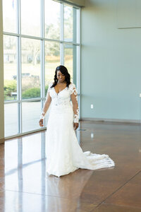 bride in white wedding gown standing in front of a wall of glass behind her