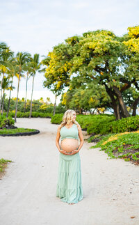 pregnant woman holding belly on the  beach. Palm trees and tropical greenery