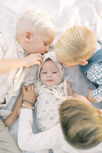 siblings huddle around their new baby sister giving her kisses and love.