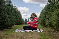 A woman sitting on the ground with her black/white small fluffy dog at the Rogish Christmas Tree Farm