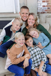 A family of six snuggled up together on the steps of a building.