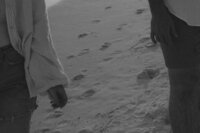 A photo of Michaela walking on the beach with her husband. A black and white photo focus on their hands with foot prints in the sand in Santa Rosa Beach Fl. 