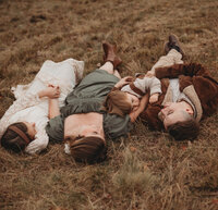 A family laying down in a field holding hands at Pipestem State Park in Princeton, West Virginia