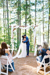 "Bride and groom embracing during their intimate, heartfelt wedding ceremony in the woods surrounded by pine trees — captured by Minnesota wedding photographer.