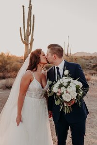 Wedding couple hold hands and kiss in front of a saguaro