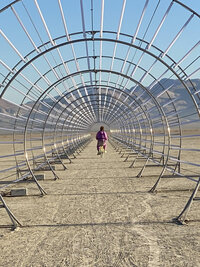 A man riding a bicycle through a cylindrical metal tunnel in the desert at Burning Man festival, symbolizing exploration, freedom, and personal transformation for seniors engaging in psychedelic coaching services.