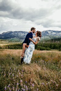 Bride in a deep red gown and groom popping champagne in a snowy forest near Lake Tahoe, celebrating their winter elopement with joy and laughter.