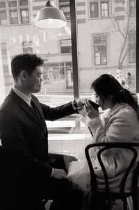 Black and white film photo of a couple sharing a quiet moment in a Boston café during their elopement — a romantic, documentary-style image by a film wedding photographer.