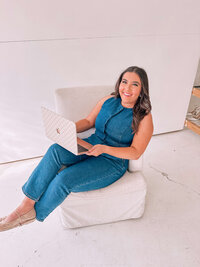 Natalie in a Denim Romper sitting on a chair with a computer