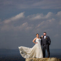 Couple standing at the Blue Mountain overlook with the sky behind them and her dress blowing in the wind.