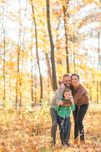 Mom and Dad hugging their son in the fall woods