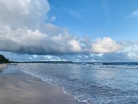 Scenic photo of the water and sand on Mayaro beach with heavy white cloud and bright blue sky overhead
