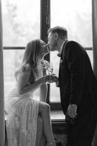 A married couple kiss in front of a window