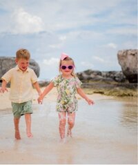 Two kids playing in clear ocean water near a sandy beach during a tropical family vacation.