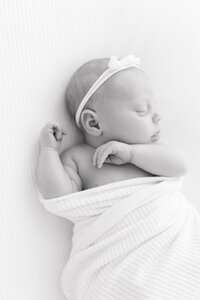 A black and white image of a newborn baby sleeping on a white blanket during her newborn photography session.