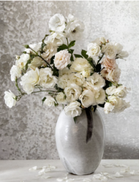 Sophisticated bouquet of white and blush flowers in a ceramic vase, styled against a textured background by Ylva Erevall.