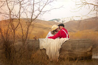 Couple sitting on log bench in fall moving in to kiss each other.