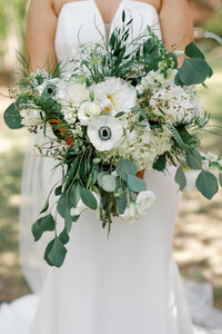 Women in white dress holding bouquet of flowers with eucalyptus leaves and white florals. 