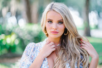 Senior girl with blonde curls wearing a blue floral top posing for elegant headshot in downtown Charleston, South Carolina