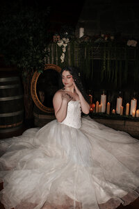 A bride in a flowing white ballgown poses gracefully in an ornate vintage chair surrounded by warm candlelight and rustic wedding decor at Cederville Lodge, capturing a timeless and romantic bridal portrait.