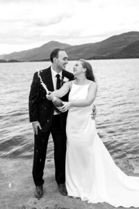 Black and white image of bride and groom standing near Lake George, NY