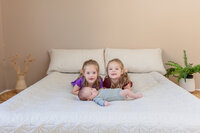 Twin girls snuggling on a bed with their newborn baby brother.