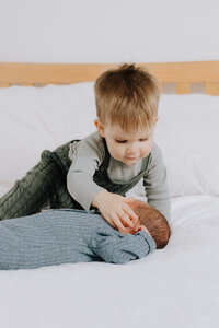 Candid moment of toddler gently stroking baby brother’s hair as he sleeps. Emotional lifestyle portrait by Nostalgia.