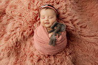 Newborn baby girl swaddled in pink with a tiny elephant plush, sleeping on a textured blanket.
Photograph by Yucaipa newborn photographer Kaitlyn Dawn Photography.