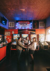 Two brides getting married in a pizza place surrounded by pinball machines. Photo by Rhode Tripper Photography