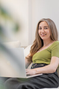 Content repurposing strategist seated on a chair with a laptop, smiling at the camera.